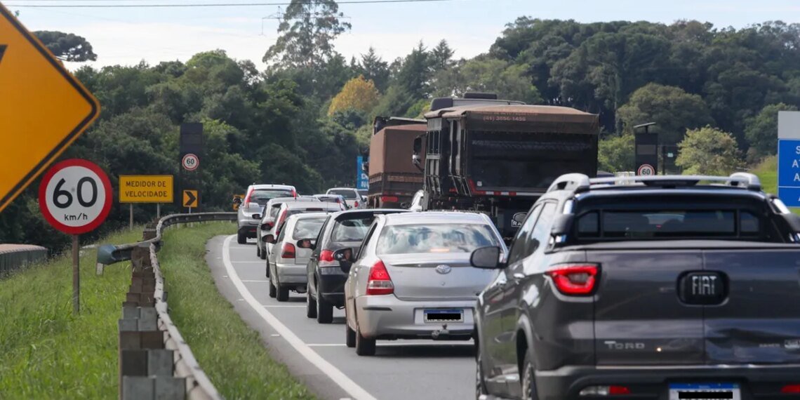 Tráfego congestionado em rodovia arborizada com carros e caminhão. Placa de limite de velocidade de 60 km/h visível.