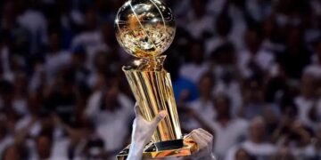 Jogador erguendo o troféu de campeão da NBA em celebração, destacando vitória no basquete em meio à multidão.