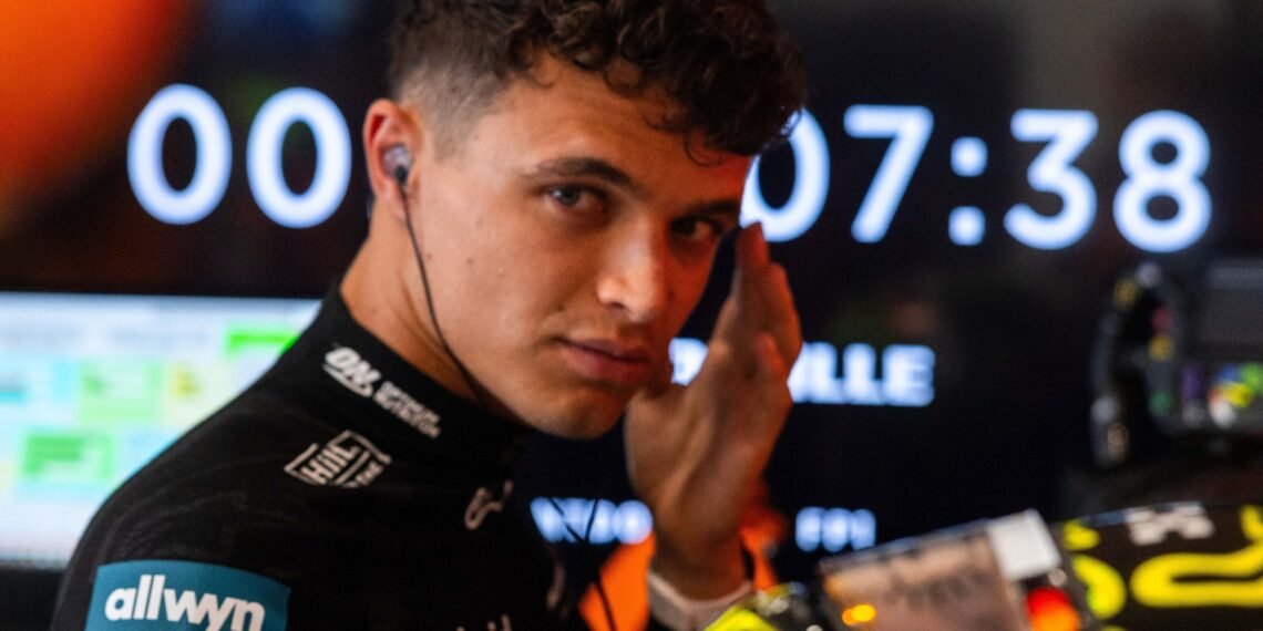 Norris reconhece falha e pede desculpas à equipe após acidente 31 Piloto de corrida concentrado nos boxes, ajustando o fone de ouvido. Ao fundo, um cronômetro digital.