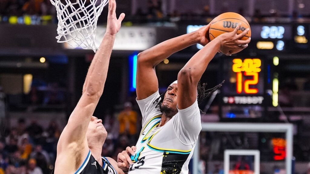 Jogador de basquete executa uma enterrada sob defesa durante uma partida intensa, capturando o dinamismo do esporte.
