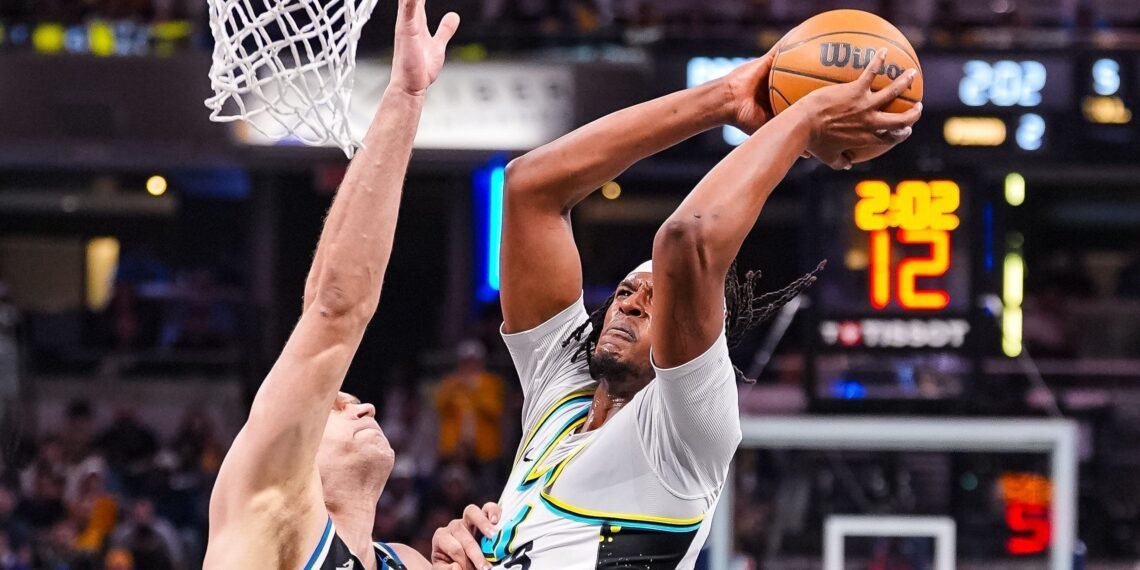 Jogador de basquete executa uma enterrada sob defesa durante uma partida intensa, capturando o dinamismo do esporte.