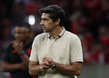 Palmeiras quebra recorde; Abel lembra Guardiola e Ancelotti 33 Treinador de futebol, concentrado, veste camisa polo bege no estádio lotado. Ambiente de competição intensa.
