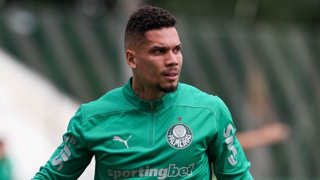 Jogador do Palmeiras em uniforme verde, observando atento ao campo, com expressão focada durante treinamento de futebol.