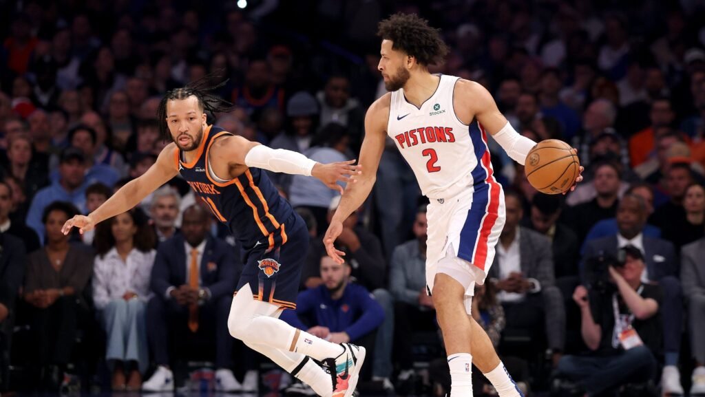 Jogadores de basquete de Knicks e Pistons disputam a posse da bola em uma partida cheia de energia e competição.