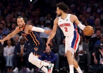 Jogadores de basquete de Knicks e Pistons disputam a posse da bola em uma partida cheia de energia e competição.