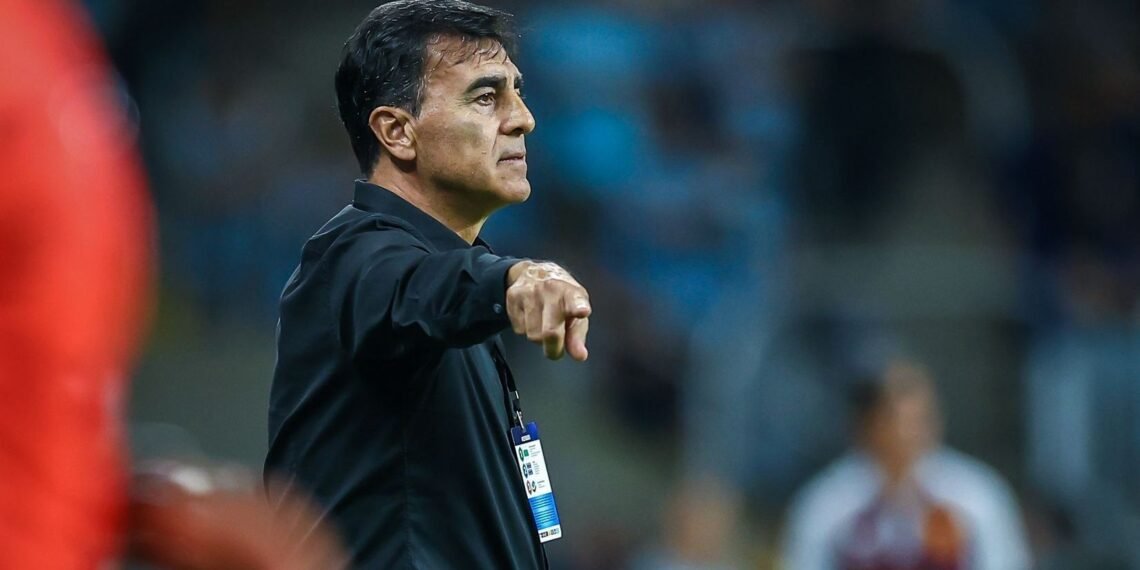 Treinador de futebol gesticula instruções à beira do campo durante partida. Atuações esportivas e táticas em destaque.