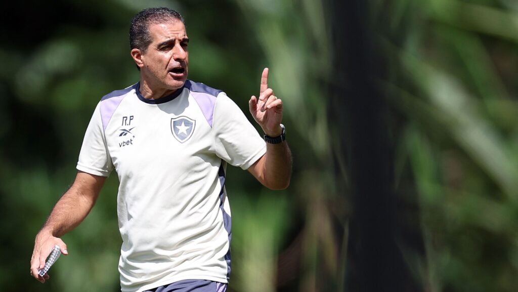 Homem com uniforme esportivo do Botafogo gesticula durante treino ao ar livre, em meio a um cenário de vegetação verde.