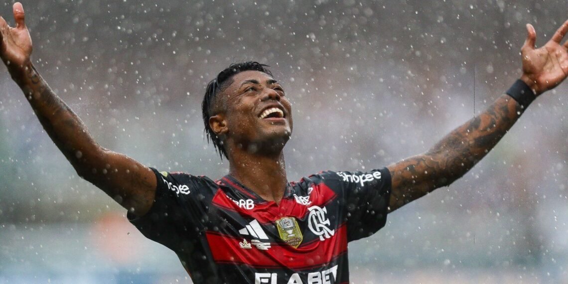 Jogador do Flamengo com expressão de vitória em campo sob chuva, braços erguidos, transmitindo emoção e energia do futebol.