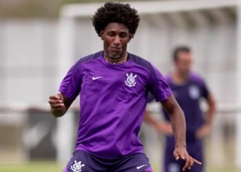 Jogador do Corinthians em campo de treino, vestindo uniforme roxo, foca no controle de bola enquanto treina com equipe.