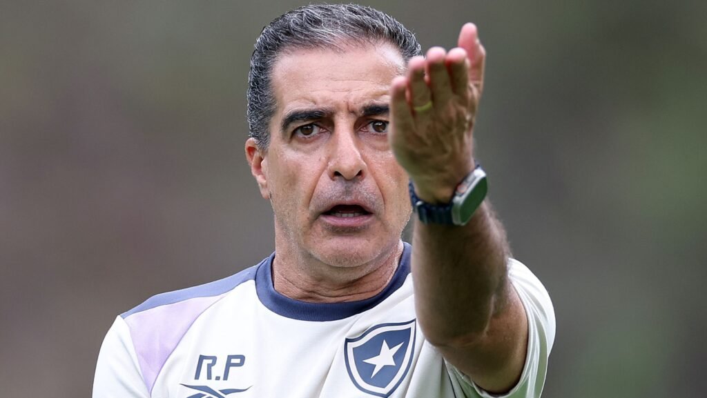 Técnico de futebol orienta jogadores durante treino, gesticulando intensamente, com expressão de foco e determinação.