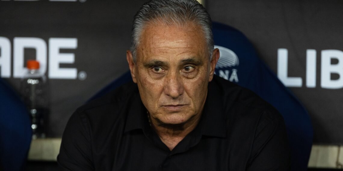 Homem de cabelos grisalhos em concentração durante evento esportivo; expressão séria, fundo com logotipo parcialmente visível.