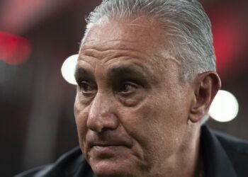 Tite e Corinthians: Entenda o 'não' que gerou ansiedade 40 Homem de cabelos grisalhos e expressão séria em um ambiente de luzes difusas vermelhas e brancas ao fundo.