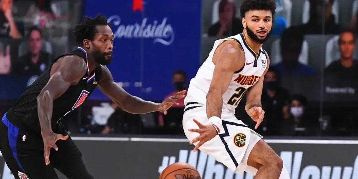 Jogador de basquete em ação desviando de marcador em partida, vestindo uniformes das equipes, com foco na bola.