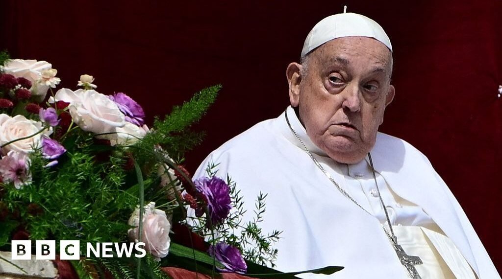Um clérigo em trajes religiosos, em frente a um arranjo de flores coloridas, observa atentamente durante um evento.