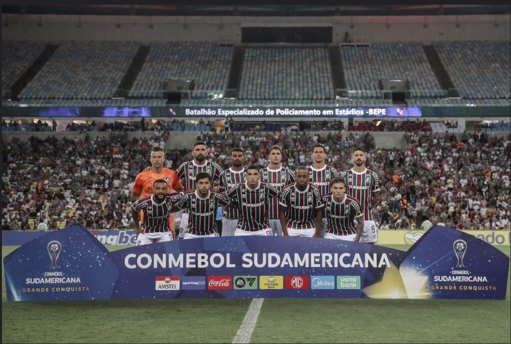 Jogadores do Fluminense posam no Maracanã para foto antes de partida da Copa Sul-americana, com grande torcida ao fundo.