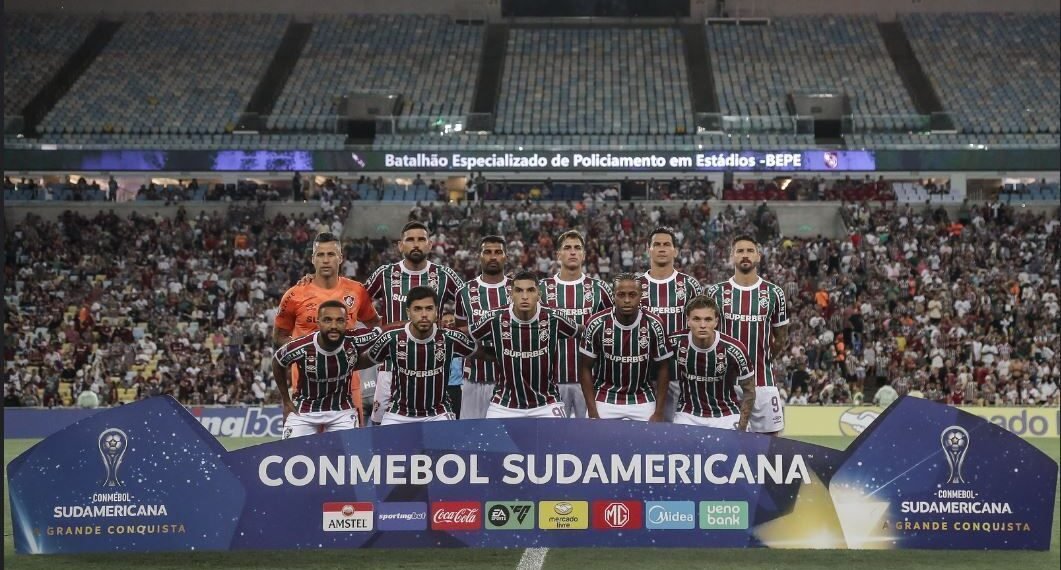 Jogadores do Fluminense posam no Maracanã para foto antes de partida da Copa Sul-americana, com grande torcida ao fundo.