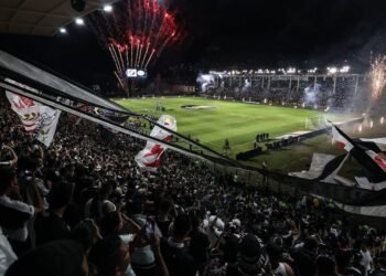 Vasco e Lanús: Horário e onde assistir à Sul-Americana 2025 35 Estádio lotado com torcedores animados empunhando bandeiras, fogos de artifício iluminam o céu durante jogo de futebol.