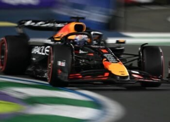 Carro de Fórmula 1 em alta velocidade em curva, destacando-se as cores preto, laranja e o número no bico do veículo.