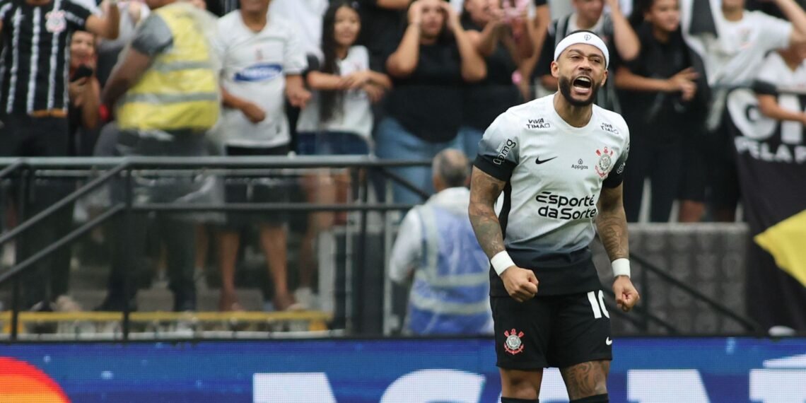 Jogador do Corinthians comemorando gol com expressão de vitória; torcida ao fundo vibra intensamente no estádio.