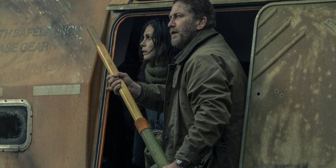 Homem e mulher saem pela porta lateral aberta de veículo militar enferrujado. Homem segura lança-foguetes enquanto ambos olham para frente com atenção.